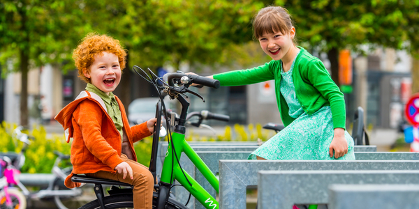 Foto van kinderen tussen fietsnietjes met een groene achtergrond.